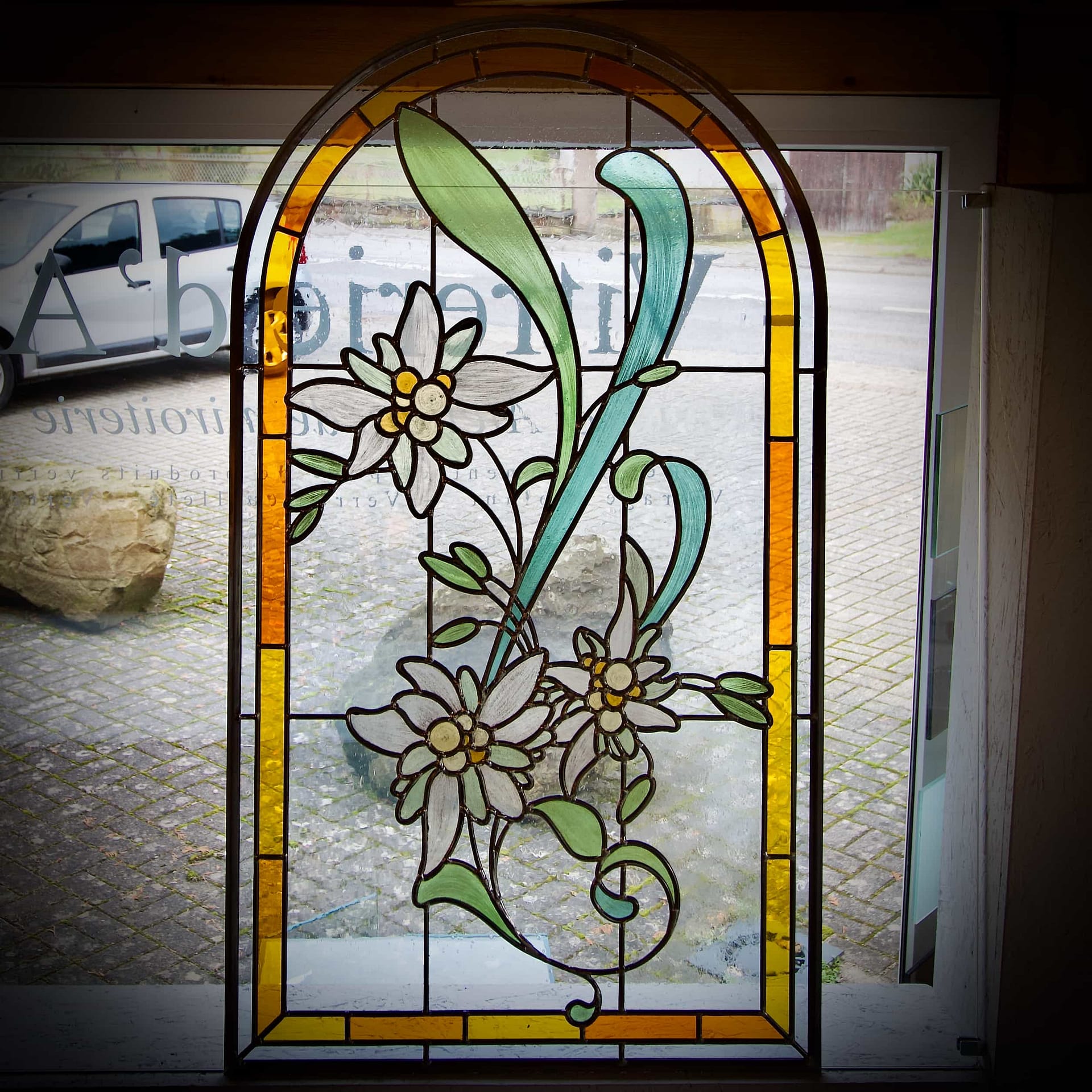 Vitrail de porte d’entrée à motif d’edelweiss, bordure ambre et arc plein cintre, en lumière transmise