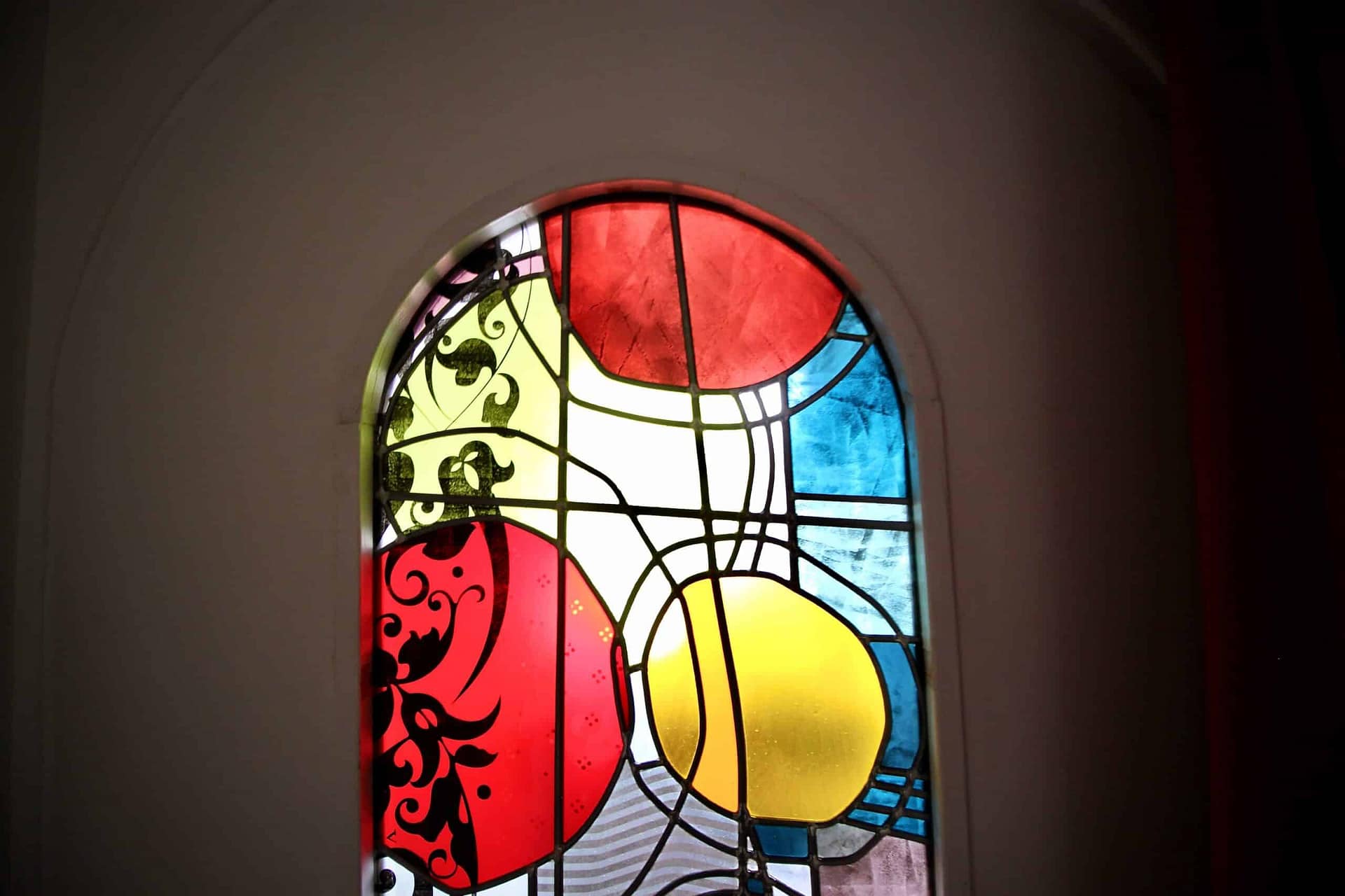 Vitrail abstrait à arc plein cintre, disques rouges, jaunes et bleus, en lumière transmise