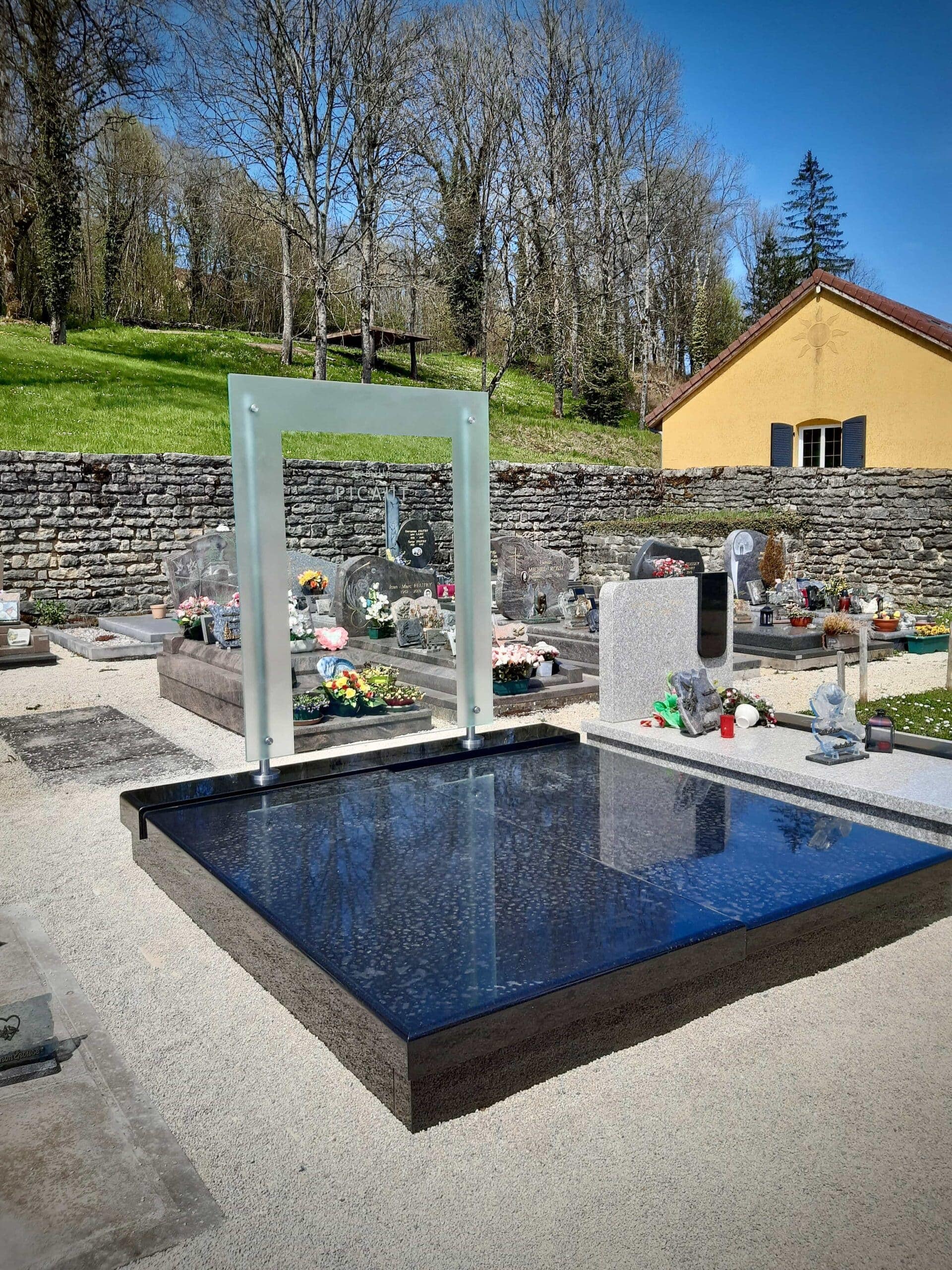 Stèle en verre en forme de cadre dressée sur une tombe de granit noir